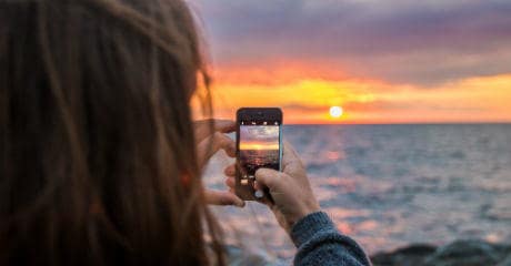Warum Eurail deine umweltfreundlichste Wahl ist | Frau macht Foto vom Sonnenuntergang mit Smartphone in Vang, Hasle in Dänemark