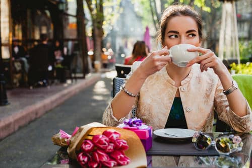 interrail_spring_trip_tile_image_-_young_stylish_woman_sitting_in_cafe_drinking_coffee_with_the_beautiful_pink_tulips_on_the_table_in_the_spring
