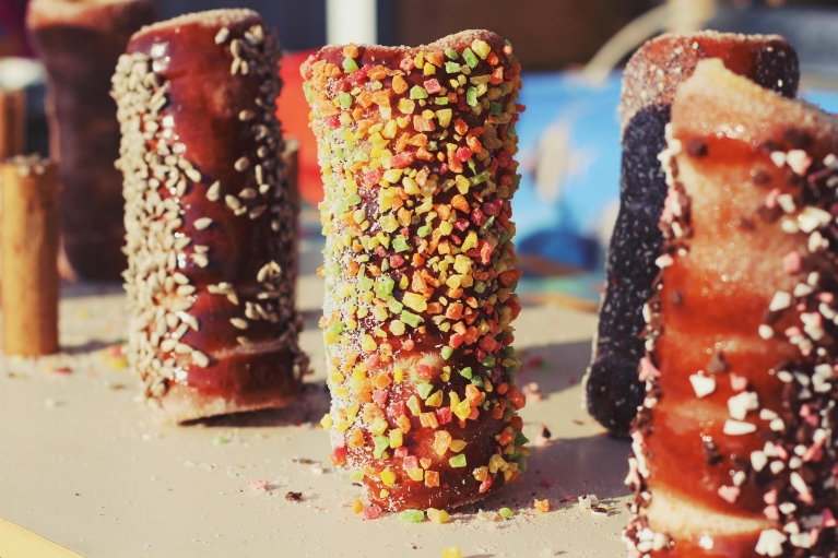 Imagen de 5 pasteles dulces húngaros en forma de chimenea, conocidos como kürtőskalács, espolvoreados con virutas