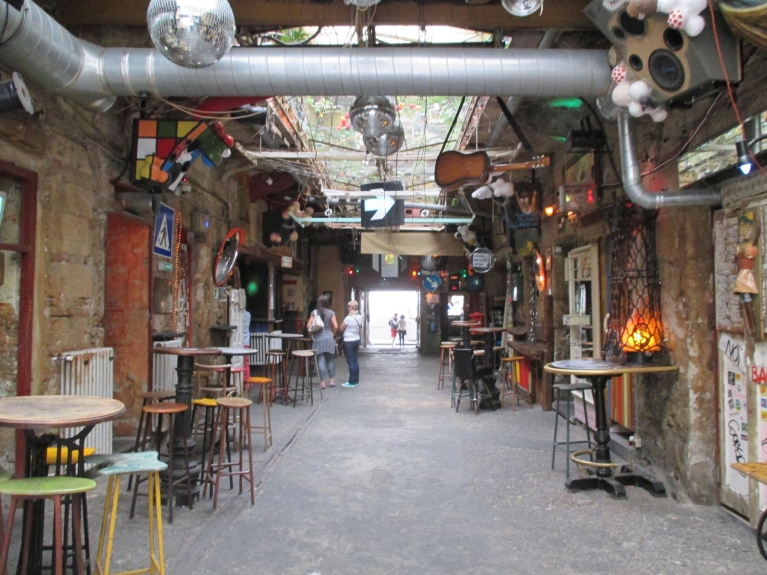 Immagine di un pub in rovina a Budapest con tavoli, sgabelli e decorazioni che pendono dal soffitto.