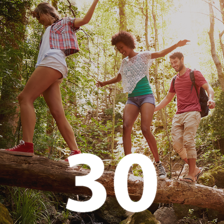 Three people walk along a fallen tree in a forest. Super-imposed is the number 30
