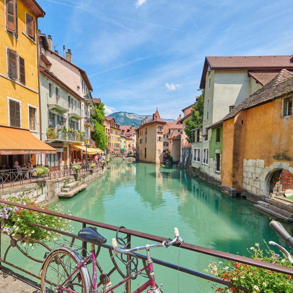 Una vista di uno dei canali blu-verdi di Annecy, con edifici gialli e bianchi su ciascun lato dell'acqua