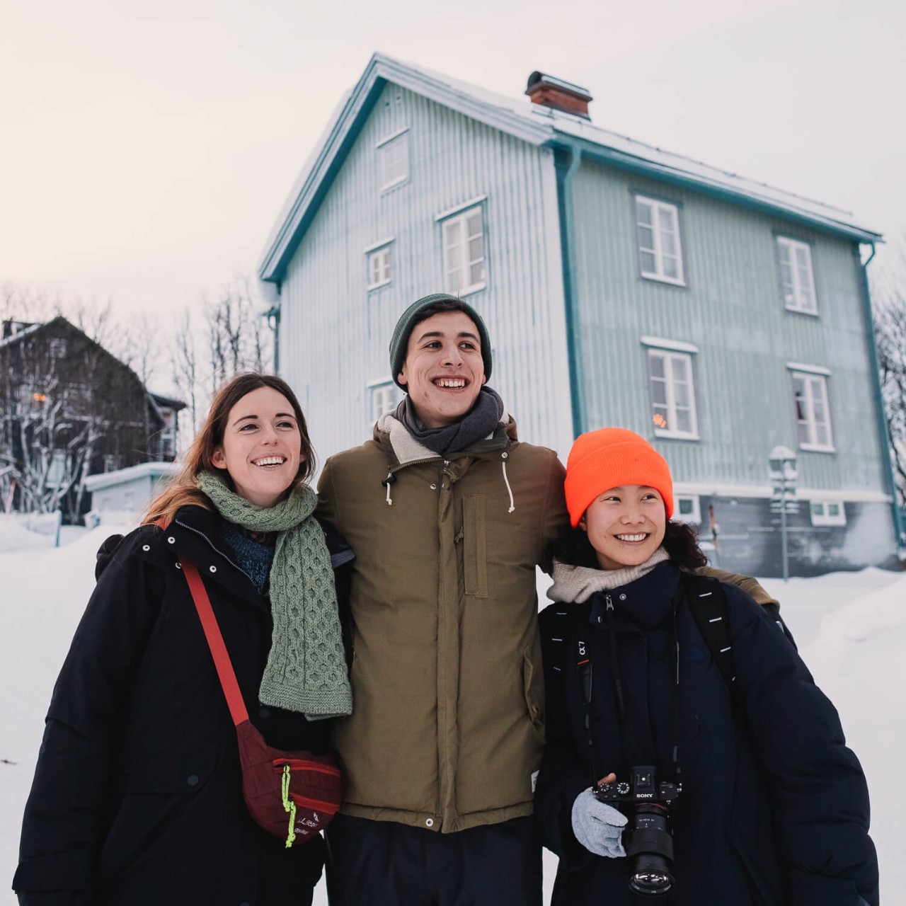 Drie mensen staan voor een blauw huis op een met sneeuw bedekte straat in Kiruna, Zweden